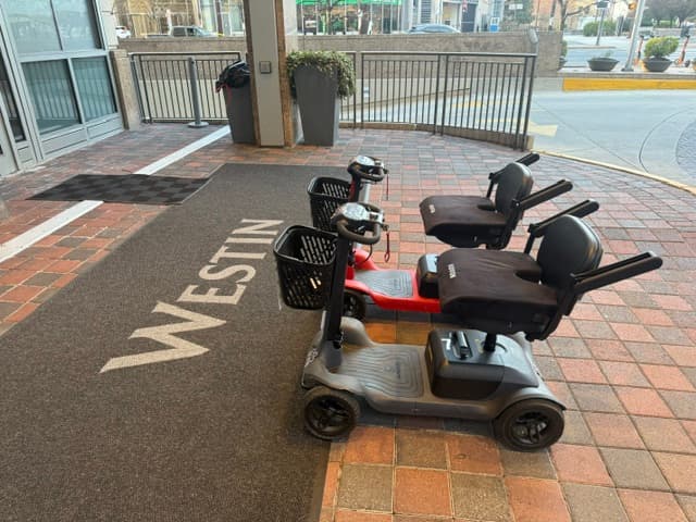 Grey and red mobility scooters parked on brick pavers outside a Westin hotel entrance.