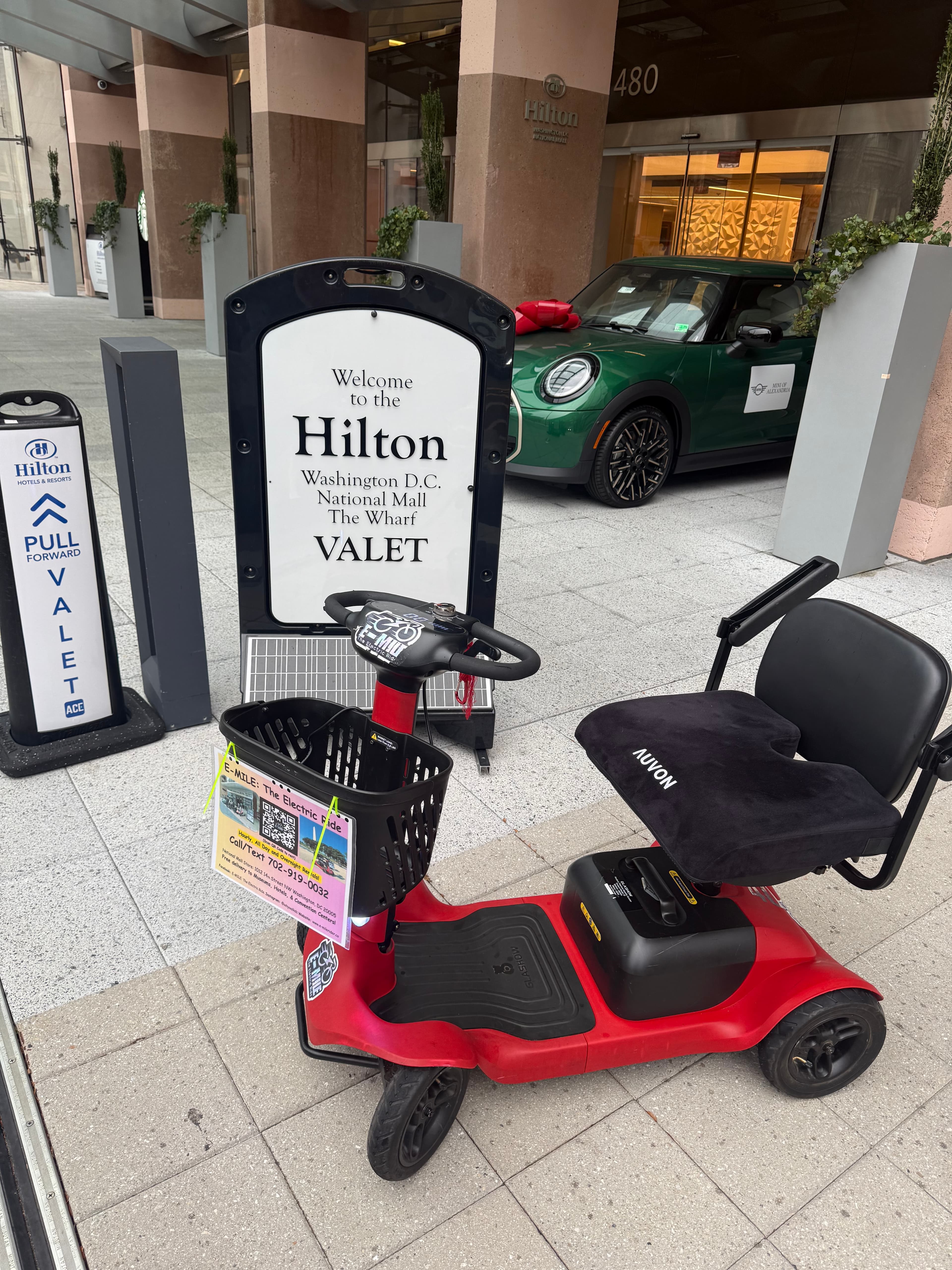 Red mobility scooter parked in front of a Hilton valet sign and a green car.